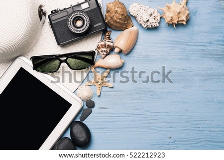 Straw hat sunglasses and photocamera among sea shells and stones on wooden surface