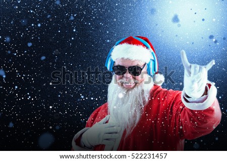 Santa claus showing horn sign while listening to music on headphones against snow with red flakes