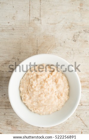 A White bowl of porridge oats or oatmeal on a natural wooden background. Shot overhead with space for copy or text Royalty-Free Stock Photo #522256891