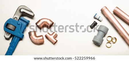 Various plumbers tools and plumbing materials including copper pipe, elbow joint, wrench and spanner. shot on a bright stainless steel background. Royalty-Free Stock Photo #522259966