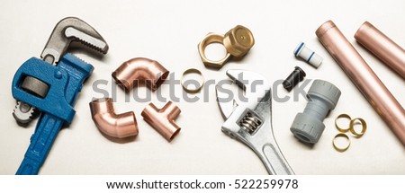 Various plumbers tools and plumbing materials including copper pipe, elbow joint, wrench and spanner. shot on a bright stainless steel background. Royalty-Free Stock Photo #522259978