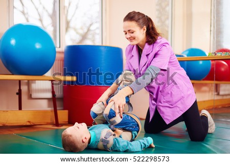 cute kid with disability has musculoskeletal therapy by doing exercises in body fixing belts