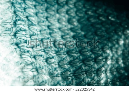 Knitted turquoise blue net texture on a dark background illuminated by light of sun. Warm scarf handmade. Abstract background. 