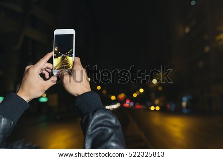 Boy takes a photograph of a street at night.