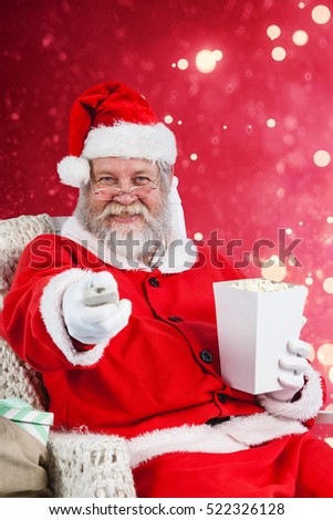 Santa Claus having popcorn while watching TV against light design shimmering on red