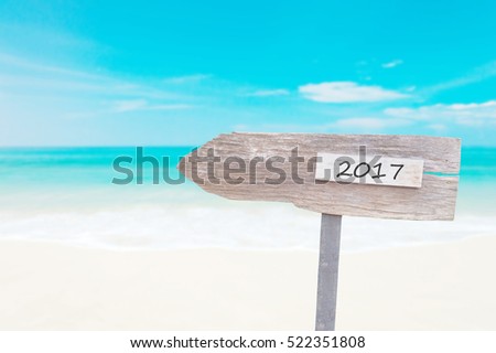 Wooden Blank Sign With Text 2017 , Over Blurred blue sea and sand beach with Cloudy Blue Sky , Image for New year 2017 Concept.