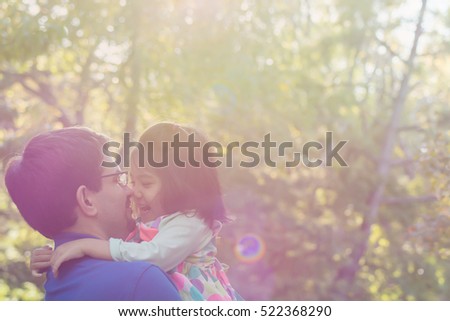 a blurred picture of father holding and playing with  a smiling little daughter with green park background