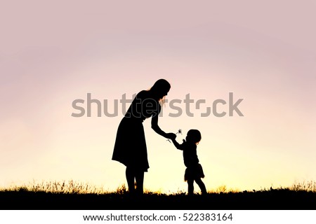 A silhouette of a sweet toddler girl is handing her mother a Daisy flower, in a meadow outside at sunset on a summer day.