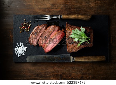 grilled steak on a black slate, knife and fork. Top view. Royalty-Free Stock Photo #522387673