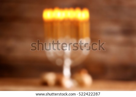 Blurred view of menorah with candles for Hanukkah on table against wooden background