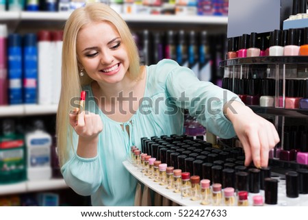 Smiling female customer buying red lipstick in makeup section  Royalty-Free Stock Photo #522427633