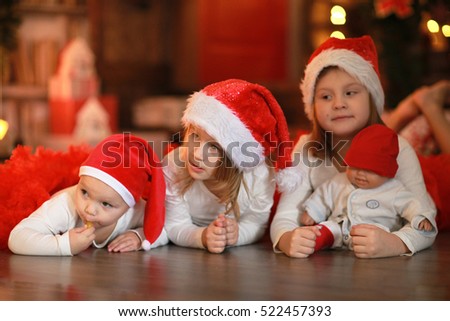 kids Siblings sisters in santa hats near the fireplace on Christmas lights background, lifestyle, soft focus, Christmas and New Year concept