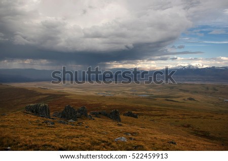 Rain from the storm dramatic dark scary clouds and a highland mountain bright steppe with rocks and stones in the foreground Plateau Ukok Altai mountains Siberia, Russia
