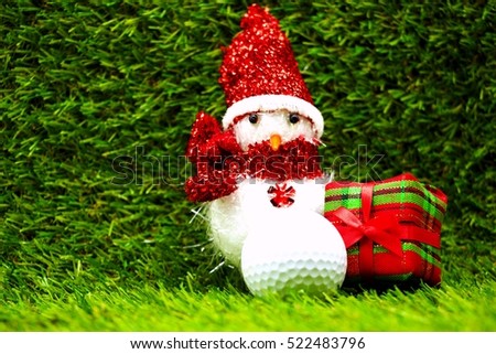 Snowman with golf ball and Christmas gift box on green grass background