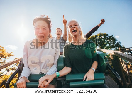 Enthusiastic young friends riding roller coaster ride at amusement park. Young people having fun at amusement park. Royalty-Free Stock Photo #522554200