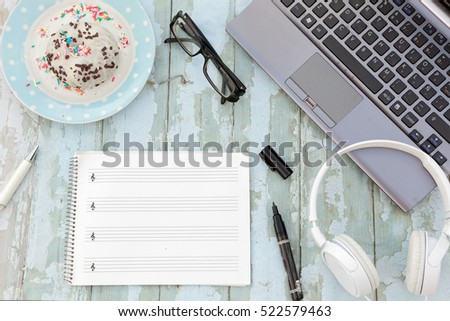 laptop, sheet music paper note notebook and laptop, headphones and donuts  on blue rustic wood background