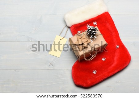 Colorful Christmas or New Year decoration include gift wrapped in craft paper with string, snowflakes and brown bow, Santa Claus red sock, pine cone and yellow tag on white vintage wooden background