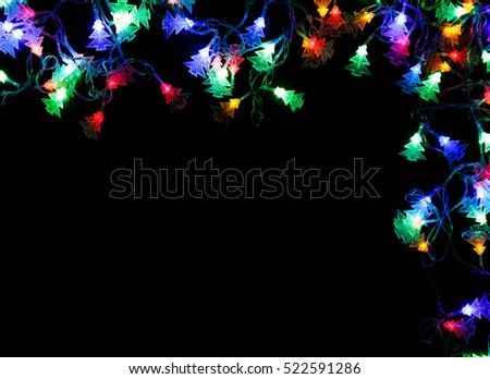 Christmas lights frame on black background. Holiday shiny garland border with copy space, top view. Xmas tree decorations, winter holidays illumination