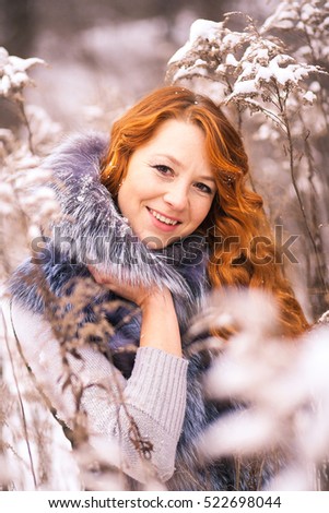 Portrait of beautiful young woman over winter snowy wood background. Closeup of female smiling face with gorgeous long ginger hair.