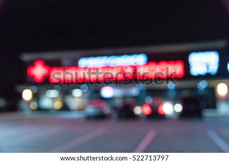 Blurred image exterior emergency room with neon led sign illuminated at night in Houston, Texas, US. Facade of emergency department with neon shining signboard and car park. Healthcare service concept