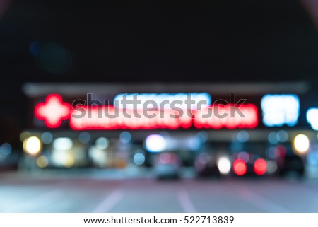 Blurred image exterior emergency room with neon led sign illuminated at night in Houston, Texas, US. Facade of emergency department with neon shining signboard and car park. Healthcare service concept