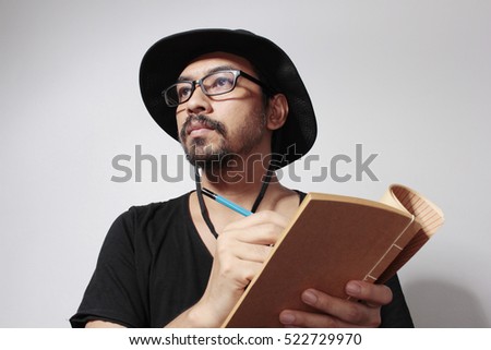 Portrait of a asian young male artist is holding a pencil and write something in note book