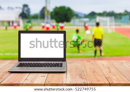 Computer on the table , blur image of football match as background.