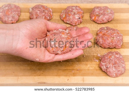 Woman's hand holding mince with grated carrots and onion in there. Cutlets creation on the wooden board in the kitchen. Healthy eating and lifestyle.