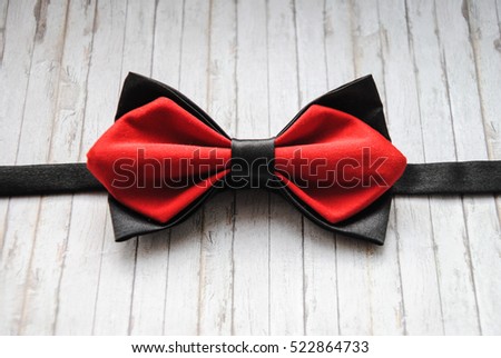 Red, black bowtie on a wooden background. Accessory for formal dress. Symbol of elegance and fashion for men. Men's casual. Men's and women's accessories. Men's and women's bow tie. Royalty-Free Stock Photo #522864733