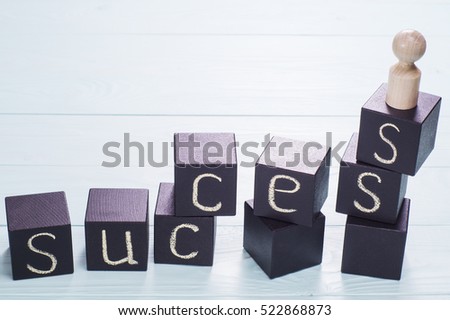 The word success written on a black wooden cubes. Abstract wooden man stands on the top of the ladder made from colorful wooden blocks. The concept of success, victories and achievements. 