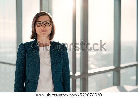 Portrait of an attractive businesswoman standing in front of windows in an office building overlooking the city