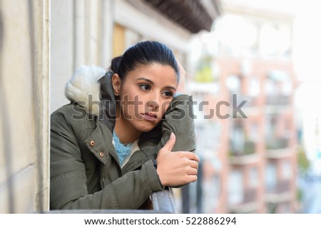young beautiful sad and desperate hispanic woman in winter coat suffering depression looking thoughtful and frustrated at apartment balcony looking depressed at the street  Royalty-Free Stock Photo #522886294