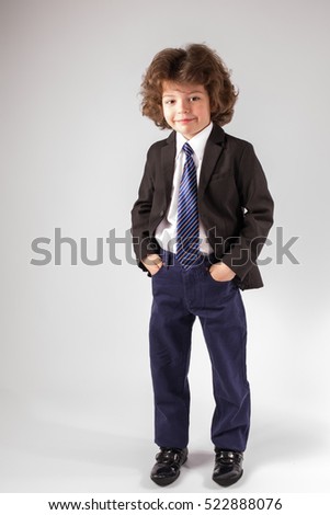 Curly cute boy standing and looking into the camera in an unbuttoned jacket. Gray background.