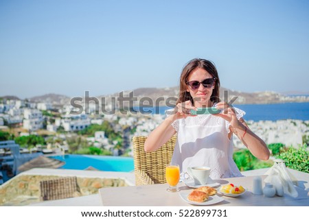 Woman taking photo of breakfast using her phone with amazing view of Mykonos. Girl taking pictures of food on luxury travel vacation for social media.