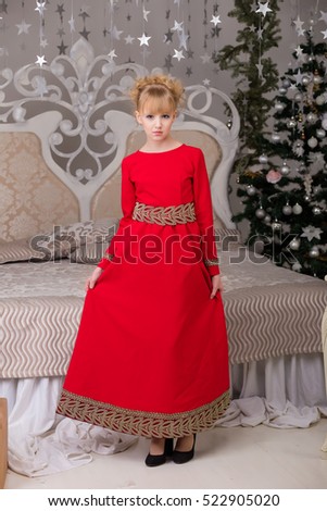 Portrait of a young beautiful blonde in a red dress at the Christmas tree. Lovely girl on the threshold of Christmas