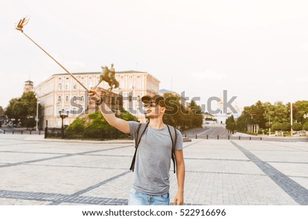 Cheerful young man in a gray shirt and a black cap with a backpack make selfie on phone in Kyiv Ukraine. Man photographing yourself with a monopod