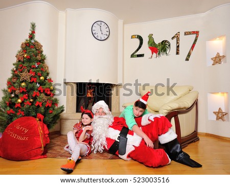 Good New Year spirit: Christmas tree, big red gift bag, fireplace and decoration for year of the rooster - Santa lay down on the floor, cute girl and his older brother in red sitting near cap  him