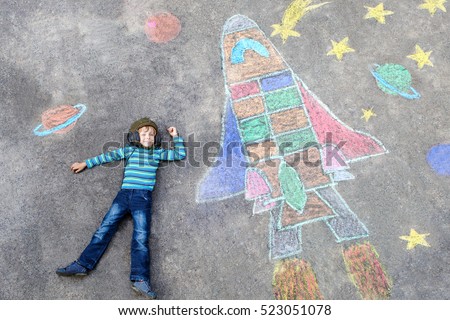 Funny little kid boy flying in universe by a space shuttle picture painting with colorful chalks. Creative leisure for children outdoors in summer.