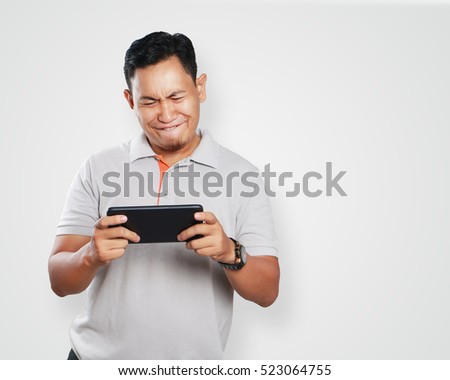 Photo image portrait of a cute handsome young Asian man with funny face playing games on tablet
