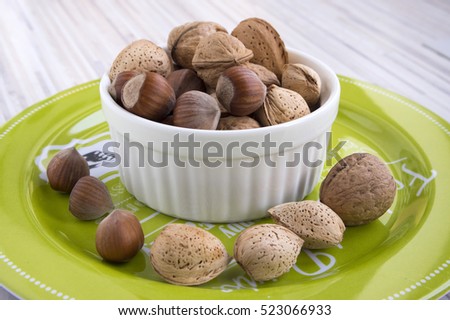 Healthy eating, various nuts in a white bowl, green plate with printed white letters and words, wooden table, Christmas decoration in the kitchen, Variety of nuts: almonds, hazelnuts, walnuts