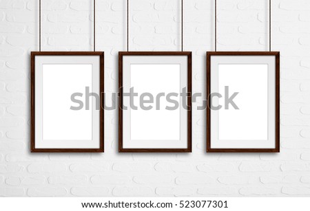 Brown natural wooden frames, hanging on cords against white bricks wall, interior decor mock up