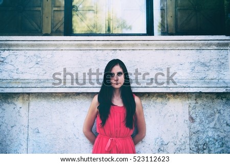 Young woman in a pink dress leaning against a marble wall. Faded and matte picture. The central composition. Really nice face and look.