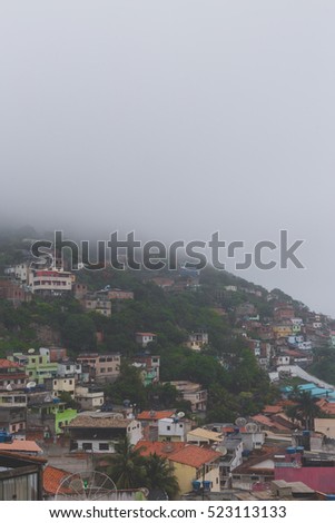 view over poor town district favela in brazil with incomplete housing for low income people, picture taken on rainy grey day, ocean coastline and overcast are on background