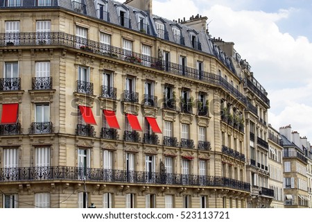Buildings at 2nd arrondissement in Paris showing 19th century architectural style. Iron, ornamental balconies and plants are in the view. Red sun screensawnings are in the view.