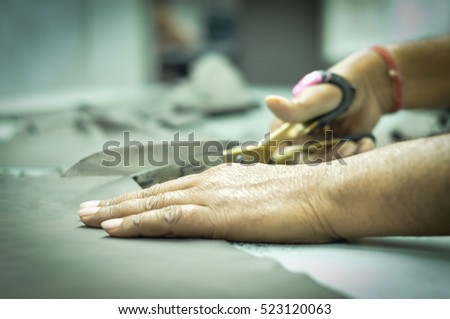 Close up of seamstress hands using scissors to cut textile at work table. Tailor cutting cloths by scissor. Only the hands of the tailor is visible. No human face visible in the image. Royalty-Free Stock Photo #523120063