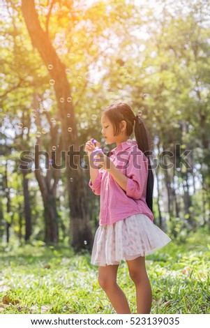 Cute little girl wearing a pink shirt blowing bubbles in the park,vintage style.
