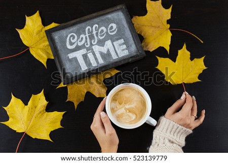 cup of cappuccino coffee while autumn leaves chalk on a blackboard