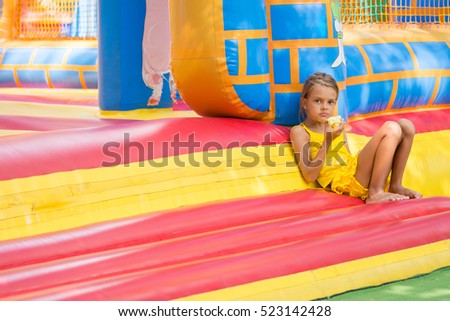 Girl sits at the entrance to an inflatable trampoline and eats an apple