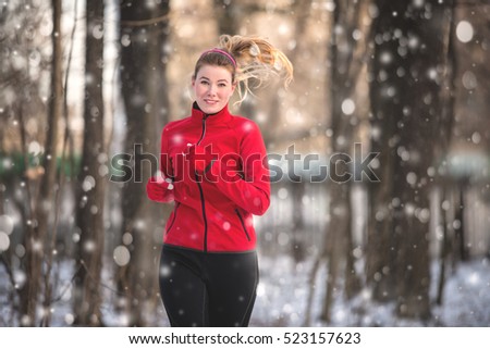 Running woman  in snowy winter park. Winter running exercise. Runner jogging in snow. Young woman fitness model running in a city park 