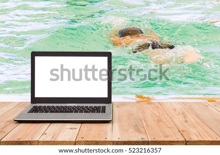 Computer on the table, blur image of swimming lessons child as background.